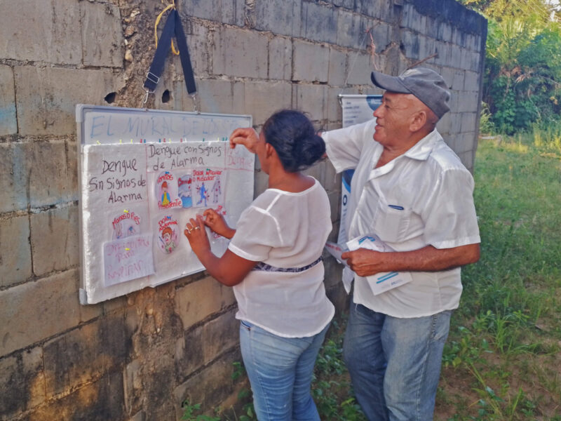 Barrio Unión community members hang a sign explaining the signs of a dengue infection.